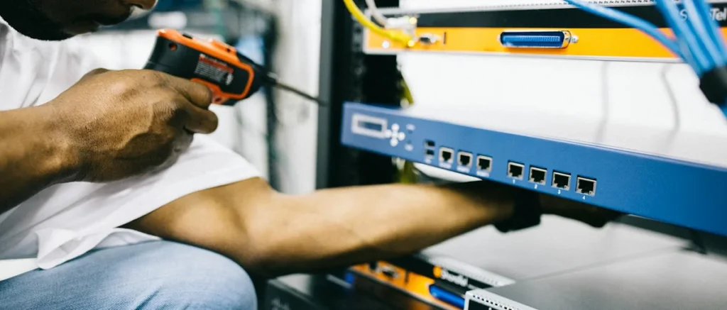 Technician working on network equipment, handling cables and tools, illustrating professional electrical and connectivity services relevant to homeowners.